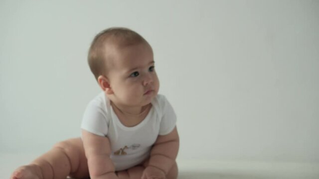 infant, childhood concept - happy funny playfull toddler kid 8 month baby girl learn to sit singly play on bed. smiling chubby active awake newborn crawl on knees indoors at home on white background
