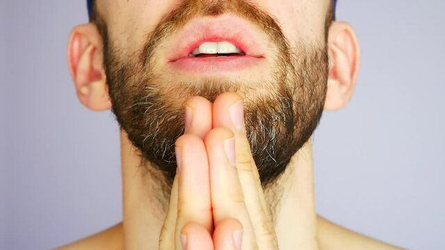 Close-up of a young bearded man praying hard against white background