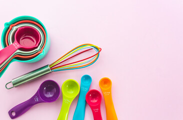 Collection of colorful measuring cups, measuring spoons and whisk use in cooking process on pink background