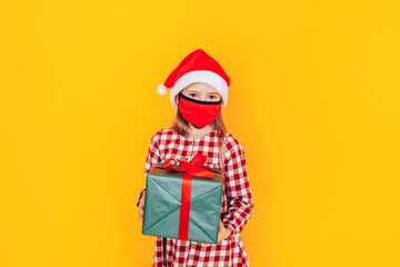 Child holding large boxes with gifts. There is a Santa hat on her head, and a medical mask on her face. Christmas mood. A perfect photo for a Christmas advertisement during a pandemic