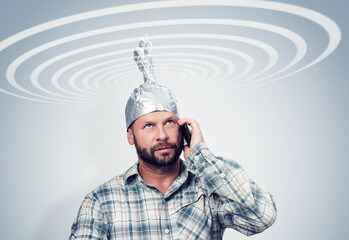 Bearded funny man in an aluminum hat talking on a smartphone with the sky, taking cosmic electric...