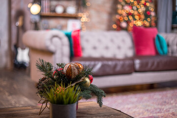 The New Year's little tree with Christmas toys at the table. Bokeh lights of the Christmas tree. Sofa with the pillow at the background.