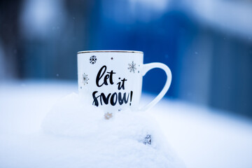 White Christmas cup on a snowdrift, blue background, outside. Mug with the inscription: "Let it snow"! Chrismas time, wintertime.