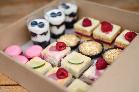 Selection of colorful and delicious cake desserts in box on table.