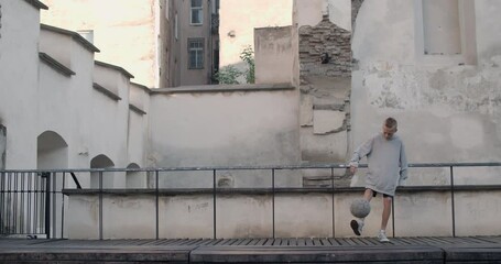 Teenager boy bouncing football ball with leg at roof of old city building. Talanted kid practicing and training in soccer tricks. Concept of lifestyle, childhood, sport