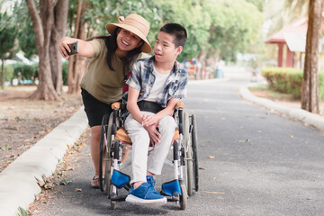 Mother and Disabled child on wheelchair fun with selfie by smart phone in the outdoor park like other people, Lifestyle of special children,Lifestyle in the education age,Happy disability kid concept.
