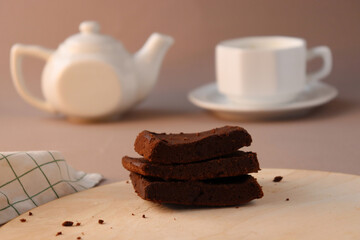Chocolate brownie on wooden board with a teapot and cappuccino. Bokeh