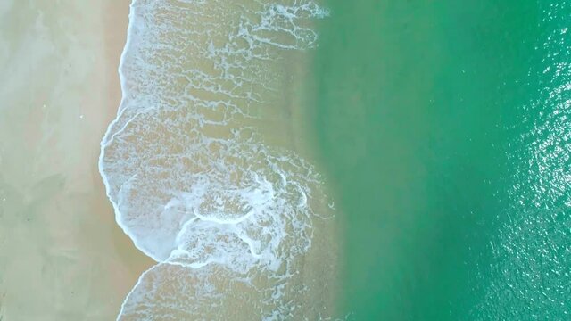 Aerial view of sandy beach and turquoise ocean. Top view of ocean waves reaching shore on sunny day.