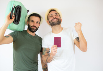 Young gay couple of two men holding suitcase going on summer vacation over white background.