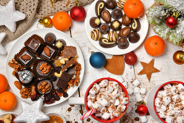 sweet food top view background for merry christmas or new year holiday decoration - chocolate candies, tangerines, cookies, marshmallow and cocoa latte on white wood
