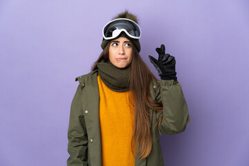 Skier caucasian girl with snowboarding glasses isolated on purple background with fingers crossing and wishing the best