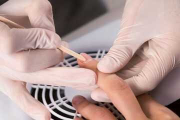Fototapeta premium Professional manicure in beauty salon. Hygiene and care for hands. Beauty industry concept. Woman manicurist master is pushing cuticle on client's fingers using wooden stick, hand closeup.