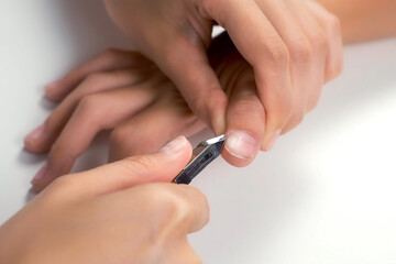Woman is cutting skin around nail on teenager boy hand using nail tongs, hands closeup. Cuts off the burrs near the nails on white background. Hygiene procedure and care for hands.