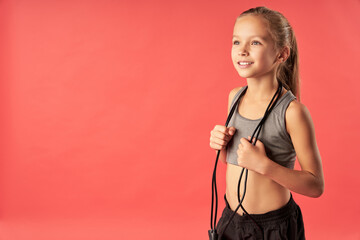 Adorable child with skipping rope standing against red background