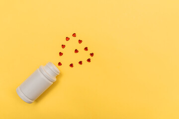 On a yellow background, a bottle and a heart made of red crystals. Valentine's day concept. Virus and disease.