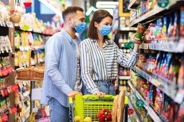 Young couple in face masks shopping in supermarket
