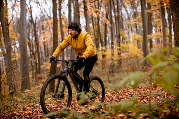 Young man biking through autumn forest