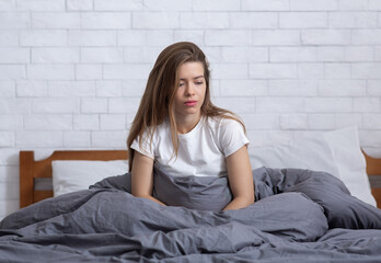 Young woman sitting alone in her bed, staring off into space, suffering from clinical depression