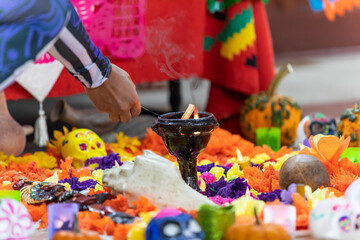 Selective focus of male hands lighting candle lying between decorated catrina and campasuchil while giving tribute during dia de los muertos