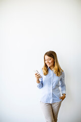 Casual young  business woman standing by the wall in the office and using mobile phone