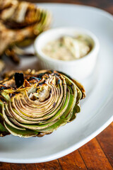 Grilled artichokes roasted in olive oil, topped with cheese sauce, garnished with scallions and Italian parsley served in cast iron skillet . Classic American restaurant or French bistro side dish.
