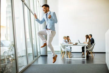 Young businessman with smartphone in a modern office jumping after receving a great news