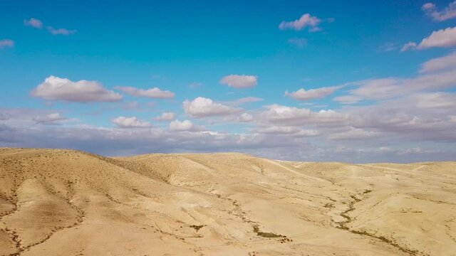 Backward flight over hills in desert Negev with fluffy clouds