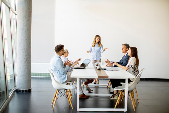 Group Of Business People With Young Adults And Senior Woman Colleague On Meeting At Modern Bright Office Interior