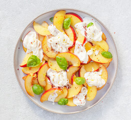 Delicious summer salad with peaches, Strachatella cheese, honey, olive oil and fresh Basil. Selective focus, top view.