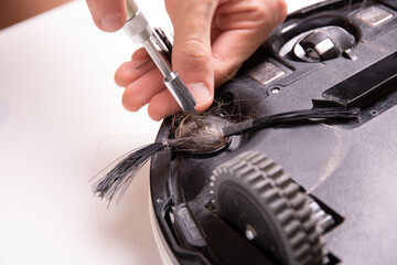 Master screwdriver unscrews the brush of a robot vacuum cleaner with hair, close-up.