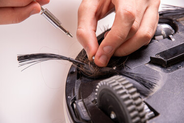 Hands of the master pull out the bolt of the brush attachment of the robot vacuum cleaner, close-up.