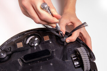 The master installs a clean brush on the robot vacuum cleaner using a screwdriver, close-up.