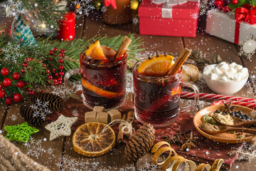 Mulled wine with orange slice, cinnamon stick on wooden background with falling snowflakes