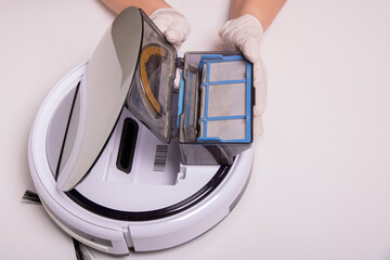 Robot vacuum cleaner on a white background above it women's hands in rubber gloves hold a container with garbage.