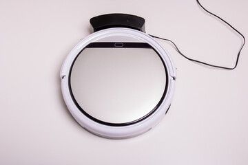 The robot vacuum cleaner is installed on a charging station with a wire on a white background.