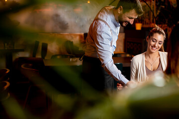 Young waiter serving food to female customers in the restaurant