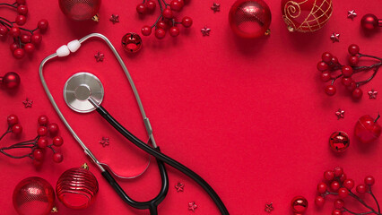 Christmas medical banner, red balls, berries, stars and stethoscope on red background top view, flat lay.Copyspace. Medicine new year flatly. Doctor writes down the text.
