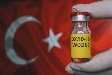 Covid Vaccine Bottle on flag Turkey background. COVID-19 Pandemic Coronavirus concept. Hand is holding the covid vaccine. Turkey Vaccination.