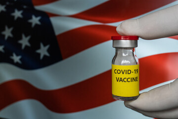Bottle vial vaccine on flag USA background. COVID-19 Pandemic Coronavirus concept. Hand is holding a bottle vaccine. United States of America Vaccination, USA flag on background.