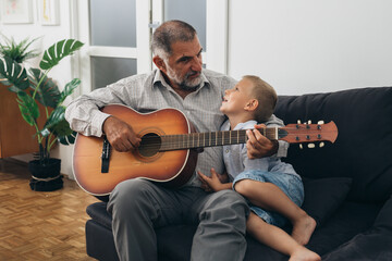 boy with his grandfather playing guitar at home