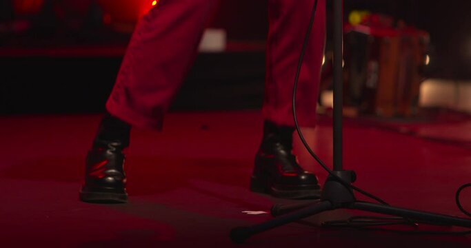 Performer singer warms up jumping neat microphone on stage red lights black boots
