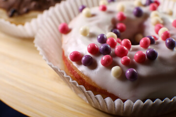 White icing donut with small colored pieces of chocolate on a wooden table against purple background