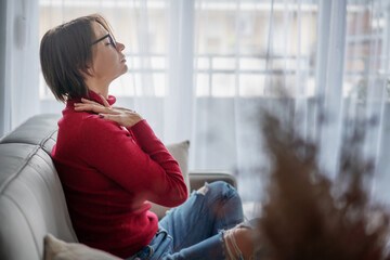 Adult woman in red sweater sitting relaxing meditating at home on sofa with closed eyes