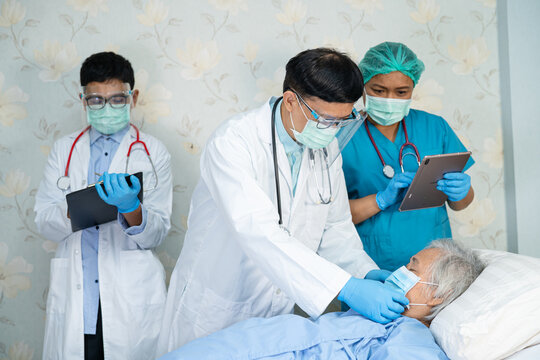 Asian doctor team check old senior lady patient for disease to motivation new normal to treat infection Covid-19 Coronavirus at hospital ward.