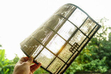 A man's hand holds a thick dirty dust filter on the air conditioner filter.