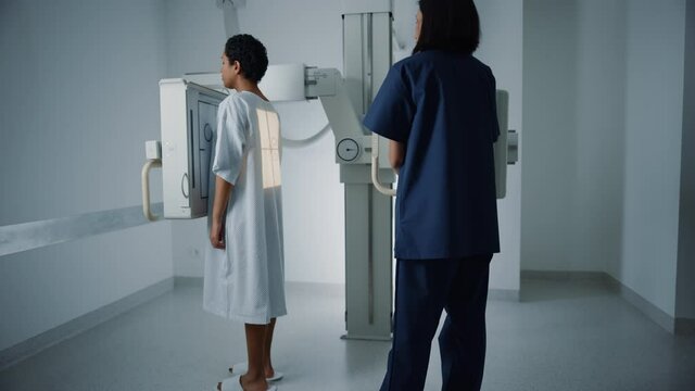 Hospital Radiology Room: Beautiful Latin Woman Standing while Female Radiologist Adjusts X-Ray Machine