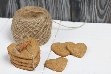 Heart-shaped gingerbread cookies tied with twine. Nearby is a cinnamon stick and a skein of string. On boards painted white. Close-up shot.