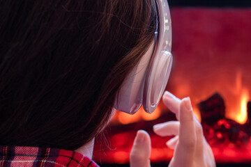 Alone sad woman in headphones sitting and warming at winter evening near fireplace flame and  christmas tree.