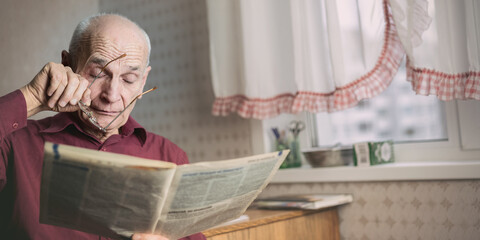 Tired elderly man holding in hands eyeglasses and newspaper and touching eye