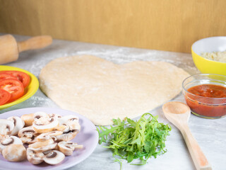 Heart shape pizza dough and ingredients on the table